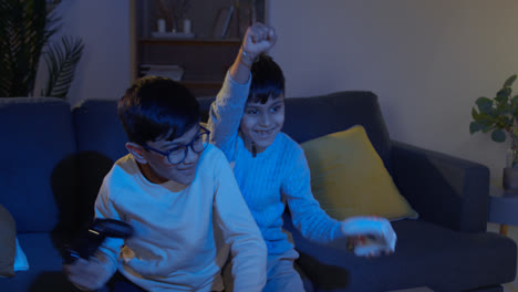 Two-Young-Boys-At-Home-Fighting-Over-Controllers-Playing-On-Computer-Games-Console-On-TV-Late-At-Night